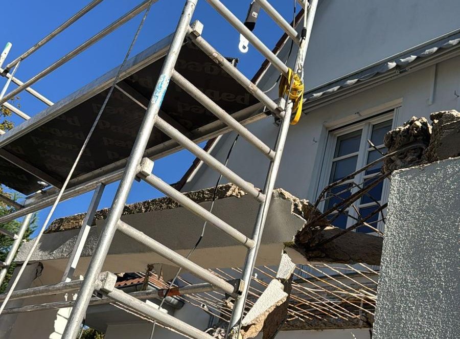 Fahrgerüst an der Hausfassade, darüber die angebrochene Betonplatte mit freigelegter Bewehrung